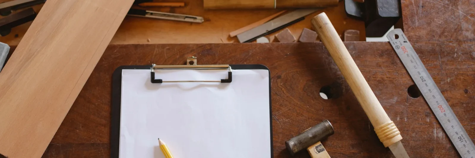 Un porte-bloc et un crayon posés sur un établi, entre une planche et un maillet